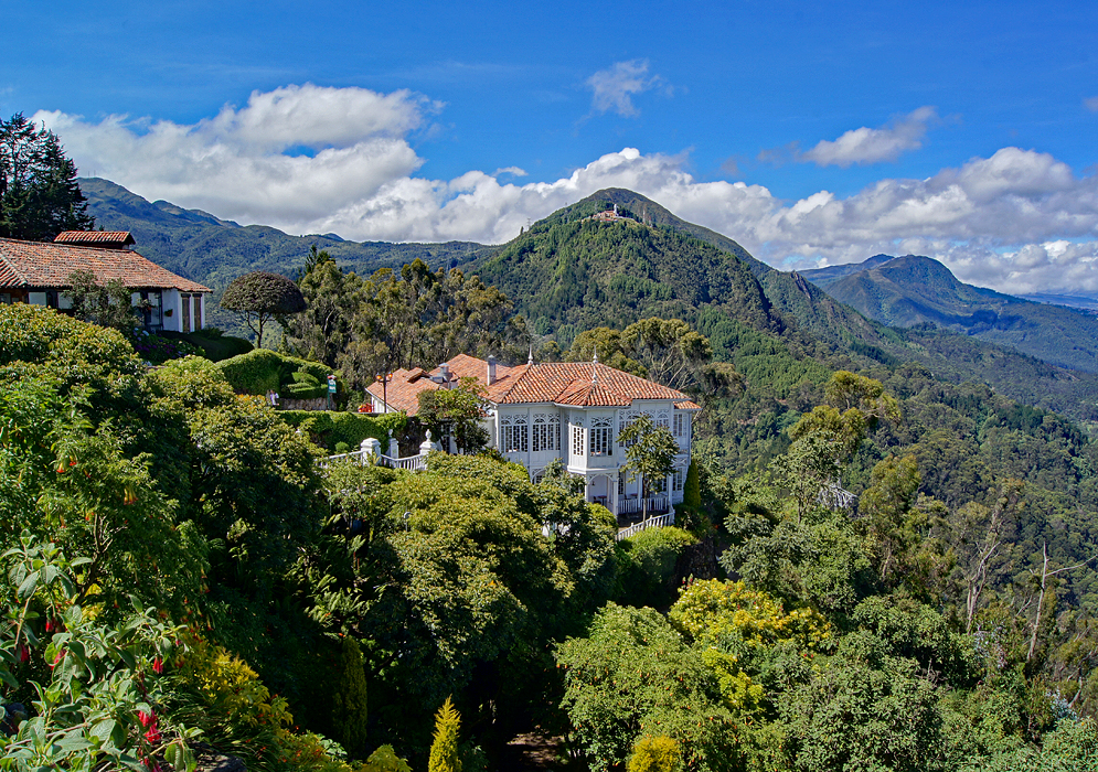 Beautiful Colombian Andes mountain scenery with blue sky and lush green trees surrounding a white hill-side restaurant
